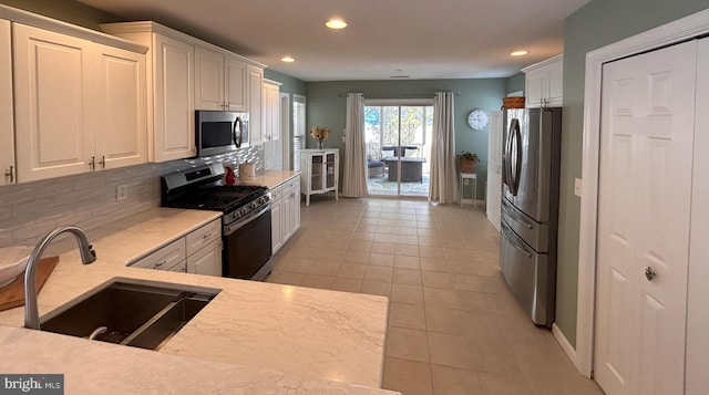 kitchen featuring white cabinets, appliances with stainless steel finishes, decorative backsplash, sink, and light tile patterned flooring