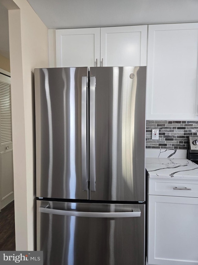 kitchen with light stone counters, white cabinets, stainless steel refrigerator, and decorative backsplash