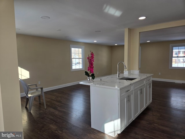 kitchen with dark wood-type flooring, sink, light stone countertops, a kitchen island with sink, and white cabinets