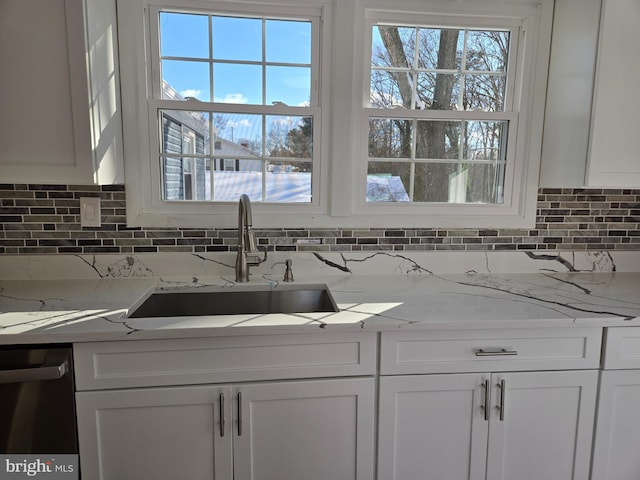 kitchen featuring dishwashing machine, sink, white cabinets, and light stone counters