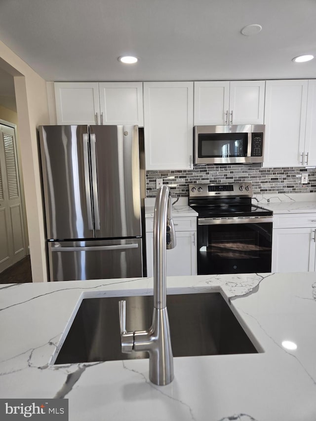 kitchen featuring light stone counters, decorative backsplash, stainless steel appliances, and white cabinets