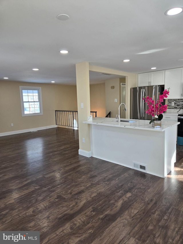 kitchen featuring white cabinetry, dark hardwood / wood-style floors, stainless steel fridge, light stone countertops, and decorative backsplash