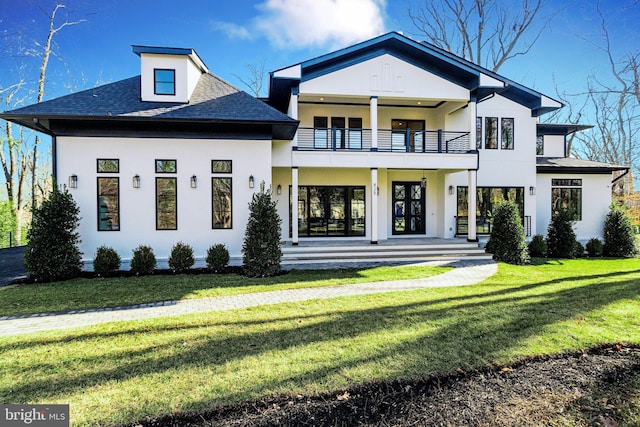 view of front of home featuring stucco siding, a balcony, a front yard, and a shingled roof