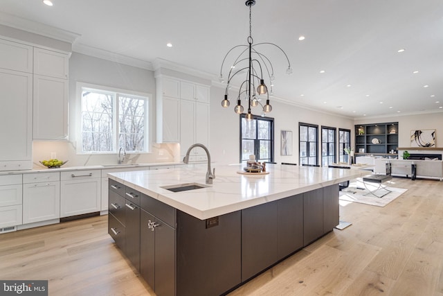 kitchen with a sink, light wood-style flooring, white cabinets, and ornamental molding