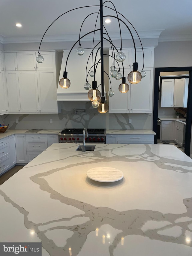 kitchen with pendant lighting, ornamental molding, a sink, light stone counters, and white cabinets