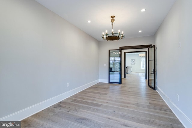 spare room featuring an inviting chandelier, recessed lighting, light wood-style floors, and baseboards