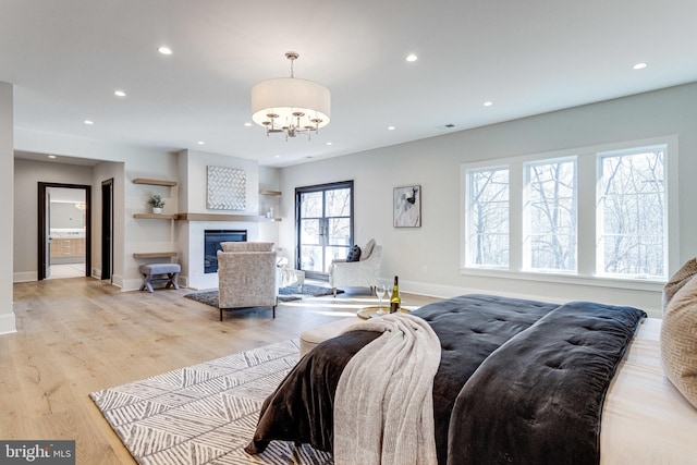 bedroom with a glass covered fireplace, recessed lighting, light wood finished floors, baseboards, and a chandelier