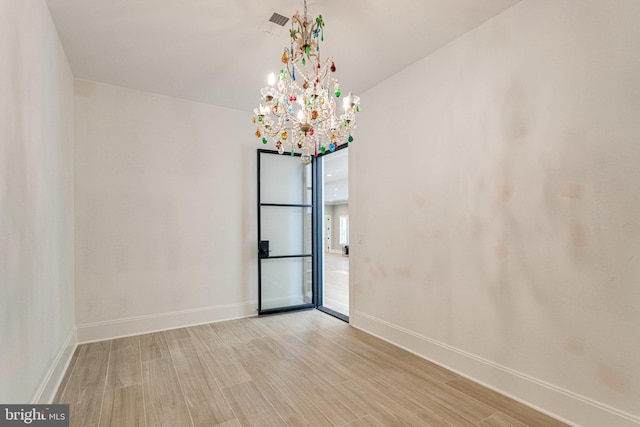 spare room featuring light wood-type flooring, baseboards, visible vents, and a chandelier