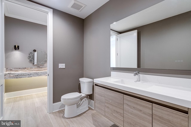 bathroom featuring visible vents, toilet, wood finished floors, baseboards, and vanity