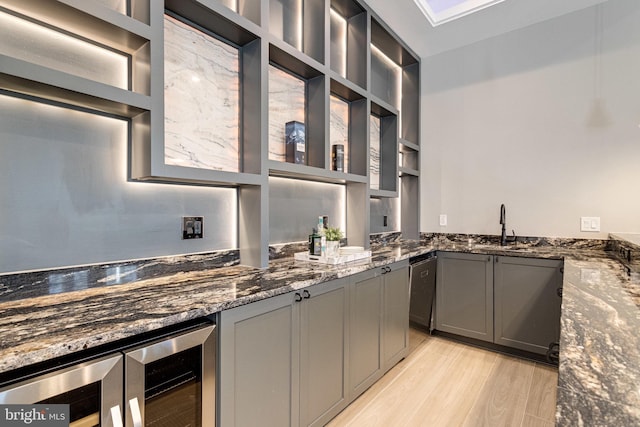 kitchen featuring beverage cooler, gray cabinets, light wood-style flooring, dark stone countertops, and open shelves