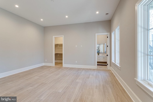 unfurnished bedroom featuring a spacious closet, recessed lighting, light wood-style flooring, and baseboards