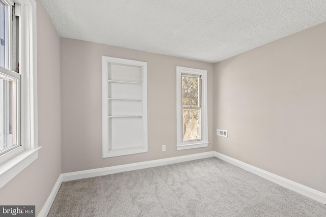 unfurnished room with plenty of natural light, carpet flooring, built in features, and a textured ceiling