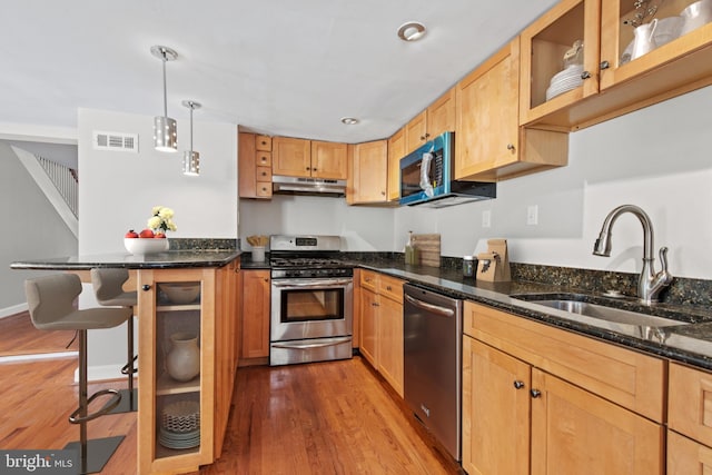 kitchen with appliances with stainless steel finishes, a breakfast bar, sink, dark stone countertops, and hanging light fixtures