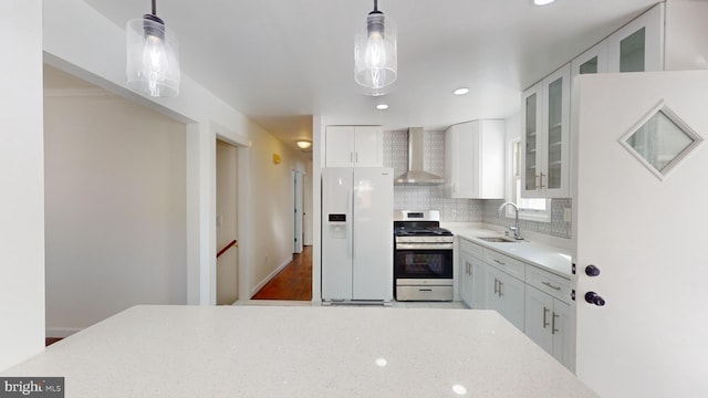 kitchen with decorative light fixtures, white refrigerator with ice dispenser, wall chimney exhaust hood, and stainless steel gas range oven