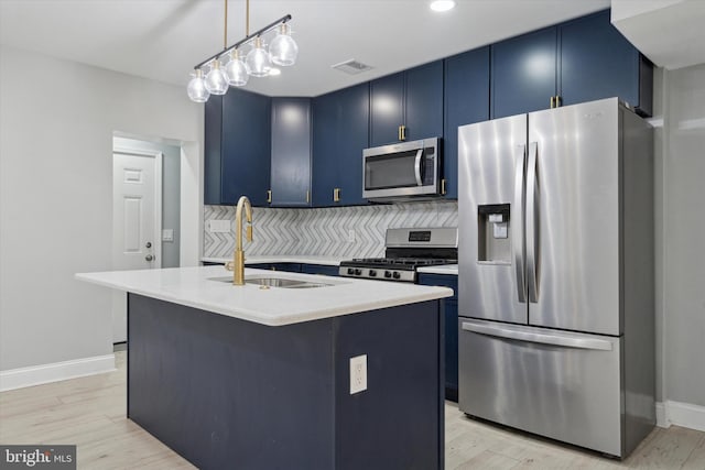 kitchen with appliances with stainless steel finishes, blue cabinets, sink, hanging light fixtures, and a kitchen island with sink