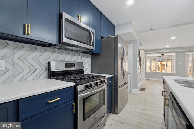 kitchen featuring appliances with stainless steel finishes, blue cabinetry, light wood-type flooring, and decorative backsplash