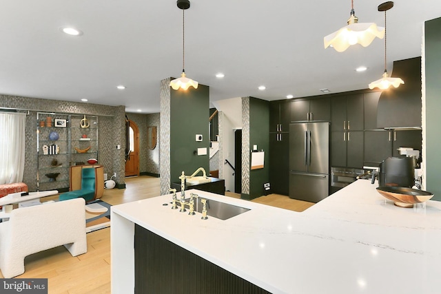 kitchen with stainless steel refrigerator, decorative light fixtures, sink, kitchen peninsula, and light wood-type flooring