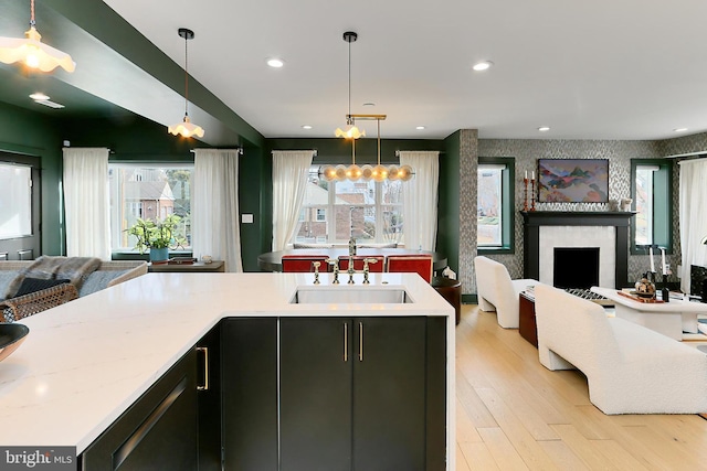 kitchen featuring dishwashing machine, sink, hanging light fixtures, light stone countertops, and light wood-type flooring