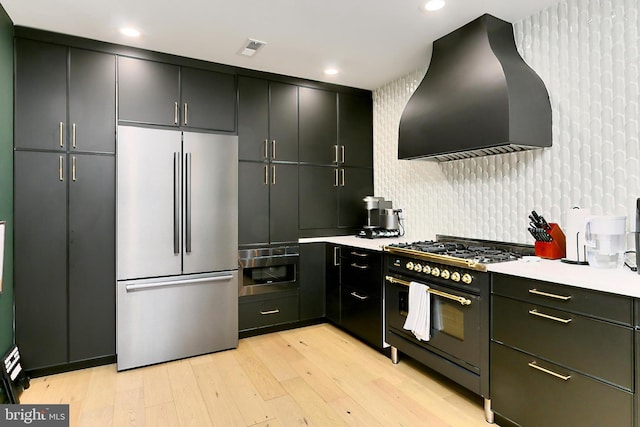 kitchen featuring stainless steel refrigerator, double oven range, ventilation hood, light hardwood / wood-style floors, and decorative backsplash