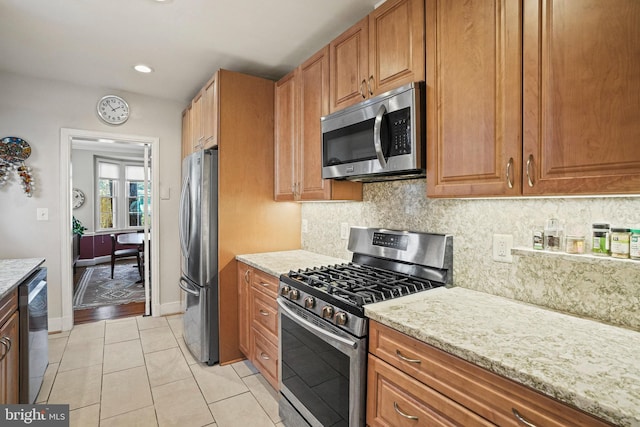 kitchen featuring appliances with stainless steel finishes, backsplash, light stone counters, and light tile patterned floors