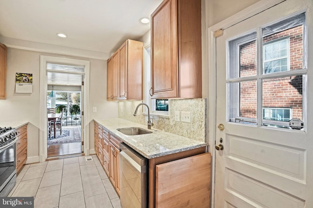 kitchen with appliances with stainless steel finishes, sink, light tile patterned floors, light stone countertops, and decorative backsplash