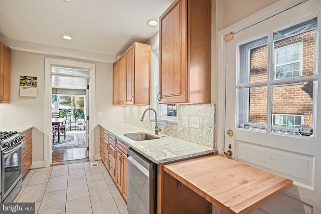 kitchen featuring sink, light tile patterned floors, appliances with stainless steel finishes, backsplash, and light stone countertops