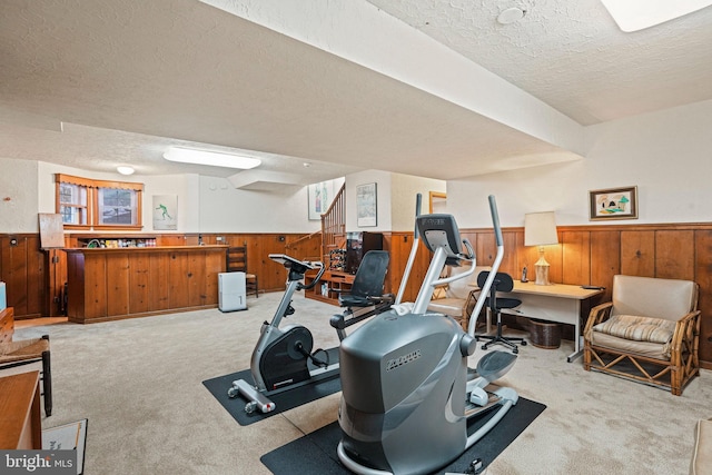 workout room featuring light colored carpet, wooden walls, and a textured ceiling