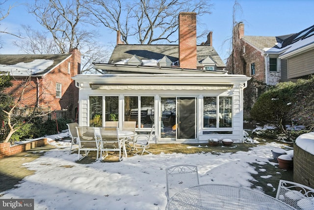 snow covered rear of property featuring a sunroom