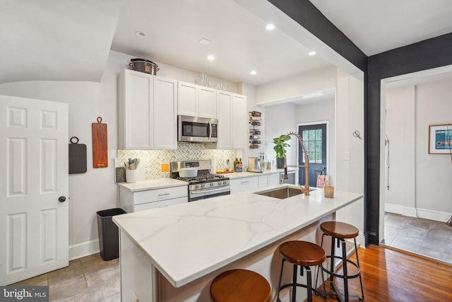 kitchen with white cabinets, appliances with stainless steel finishes, a center island with sink, and a breakfast bar