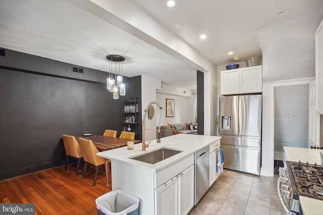 kitchen featuring appliances with stainless steel finishes, a kitchen island with sink, pendant lighting, white cabinets, and sink