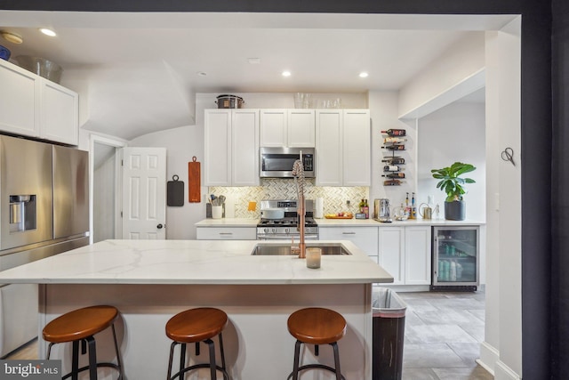 kitchen featuring white cabinetry, stainless steel appliances, backsplash, wine cooler, and light stone countertops