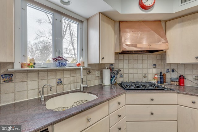 kitchen featuring sink, backsplash, black gas cooktop, and wall chimney range hood