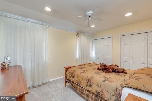 bedroom with ceiling fan, light colored carpet, vaulted ceiling, and two closets