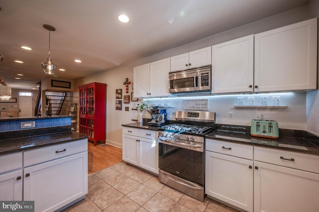 kitchen featuring hanging light fixtures, dark stone countertops, light tile patterned floors, stainless steel appliances, and white cabinets