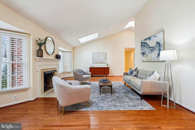 living room with wood-type flooring, a premium fireplace, and vaulted ceiling with skylight