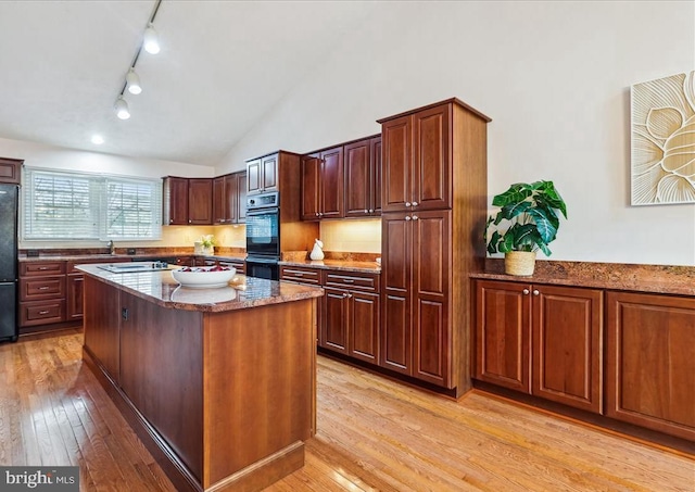 kitchen featuring multiple ovens, a center island, vaulted ceiling, light wood-type flooring, and black refrigerator