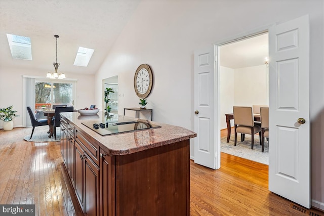 kitchen featuring an inviting chandelier, a kitchen island, pendant lighting, black electric stovetop, and hardwood / wood-style floors