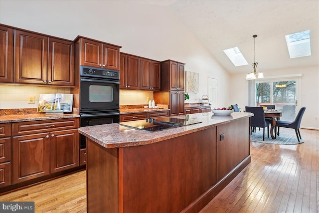 kitchen with decorative light fixtures, a skylight, an island with sink, light hardwood / wood-style floors, and black appliances