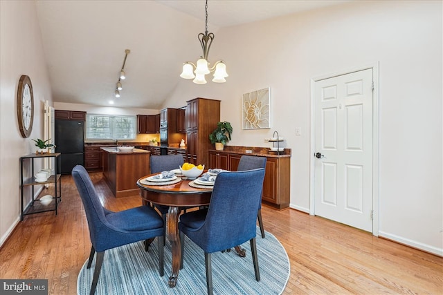 dining area featuring sink, a chandelier, vaulted ceiling, track lighting, and light hardwood / wood-style floors