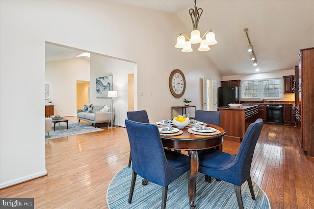 dining space featuring high vaulted ceiling, sink, an inviting chandelier, and light wood-type flooring