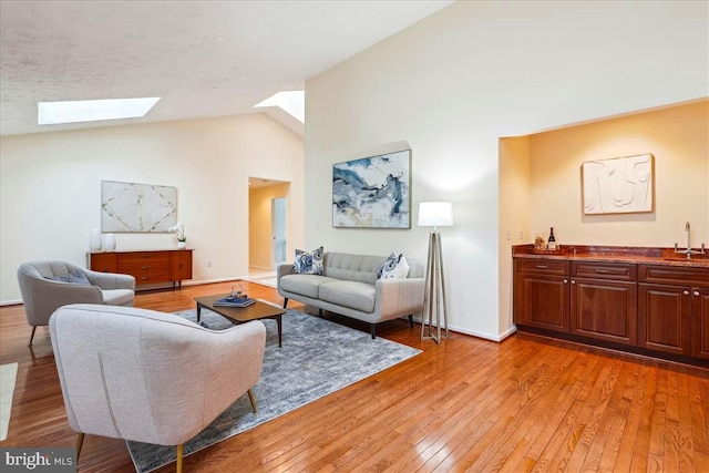 living room featuring sink, light hardwood / wood-style flooring, high vaulted ceiling, and a skylight