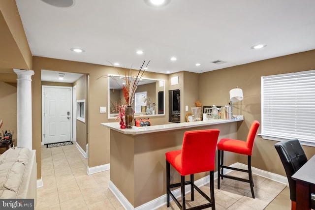 kitchen featuring ornate columns, a breakfast bar area, light tile patterned floors, and kitchen peninsula