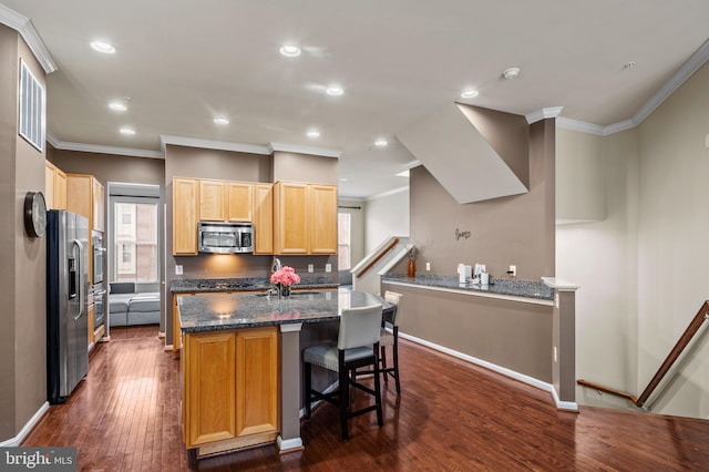 kitchen featuring appliances with stainless steel finishes, a kitchen breakfast bar, a center island, dark hardwood / wood-style flooring, and dark stone counters