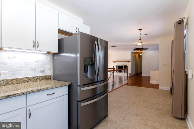 kitchen featuring light stone counters, hanging light fixtures, stainless steel fridge, and white cabinets