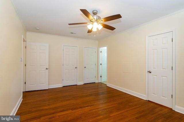 unfurnished bedroom featuring crown molding, ceiling fan, multiple closets, and dark hardwood / wood-style flooring