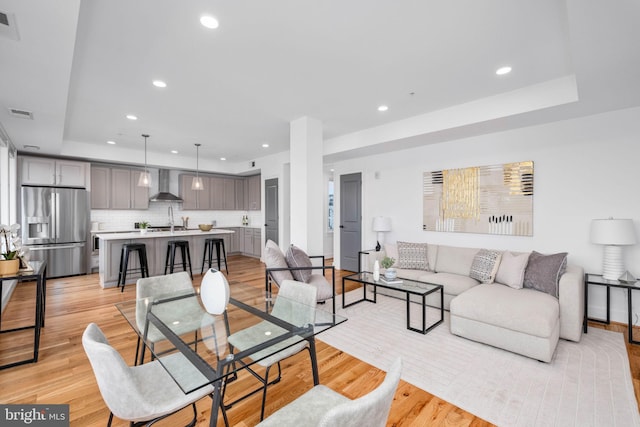 living room featuring sink, light hardwood / wood-style floors, and a tray ceiling