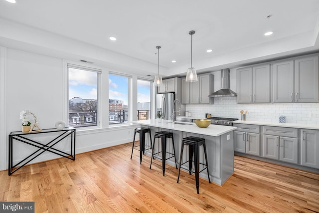 kitchen featuring a kitchen breakfast bar, light hardwood / wood-style flooring, appliances with stainless steel finishes, wall chimney exhaust hood, and a kitchen island with sink