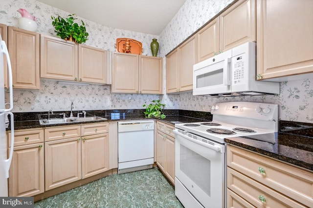 kitchen with white appliances, dark stone counters, light brown cabinetry, and sink