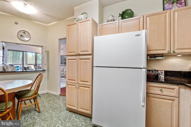 kitchen featuring dark stone counters, a textured ceiling, white fridge, and light brown cabinets