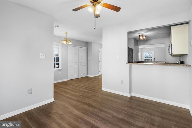 unfurnished living room featuring dark wood-type flooring and ceiling fan with notable chandelier